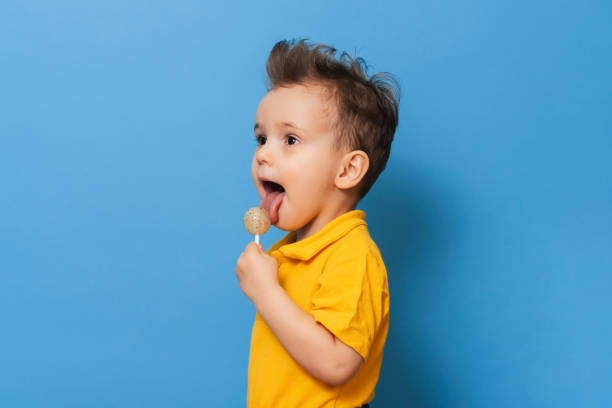 charming boy looks at the camera while holding a lollipop on a blue background. Prevention of childhood caries