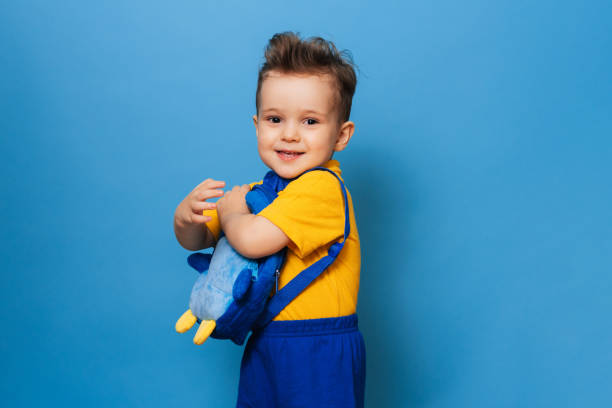 istock Cute little one cuddles with his backpack on a blue background. Funny kid 2153089988