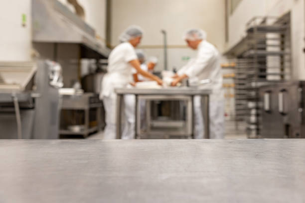 Focus on foreground on a kitchen counter and a team of bakers working at an industrial bakery at the background