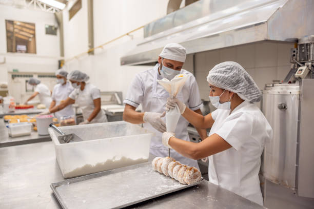 istock Baker supervising a worker filling donuts at an industrial bakery 2153090662