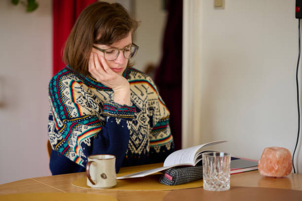 istock Young woman sitting at her kitchen table with a book 2153091679
