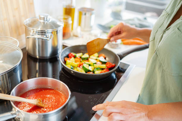 Woman adjusting temperature in a stove top while cooks vegetables