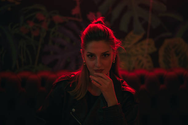 A young woman sits in a dark lounge, illuminated by red neon light.