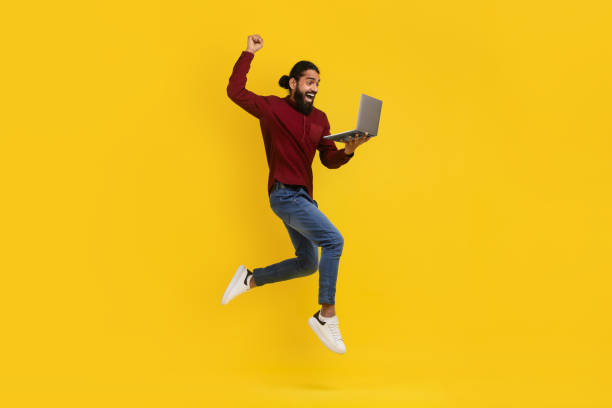 istock Excited eastern man jumping up with laptop in his hand 2153098430