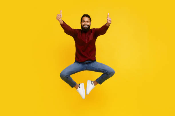 istock Joyful Man Jumping With Thumbs Up Against Vibrant Yellow Background 2153098455