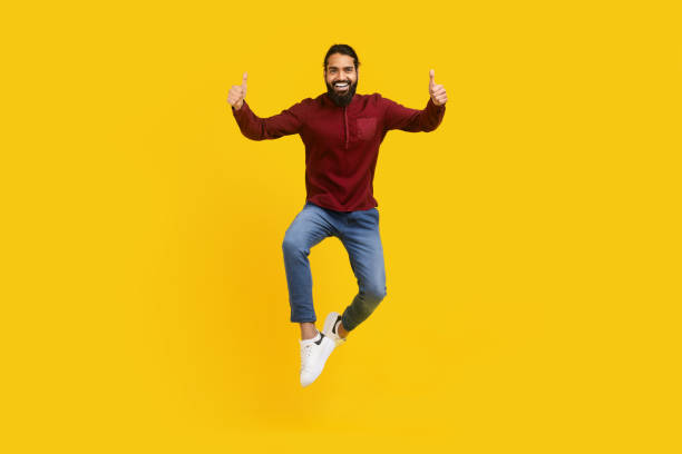 istock Man Jumping in the Air With Hands Raised on Yellow 2153098487