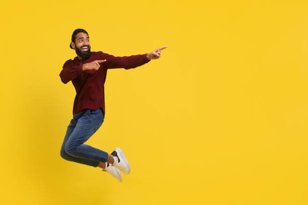 istock Emotional excited millennial indian guy jumping, showing advertisement 2153098541