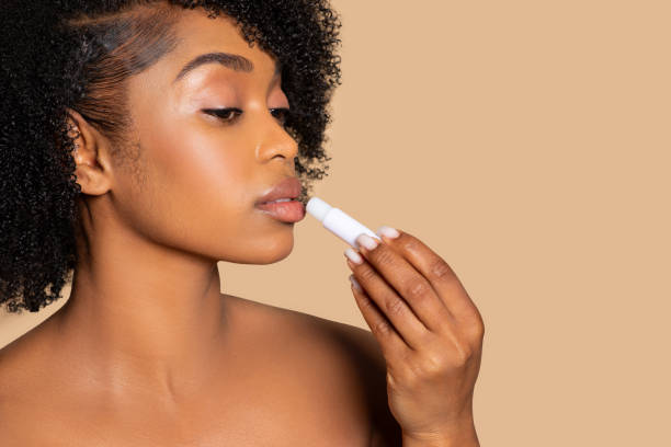 istock Black woman applying lip balm, close-up on beige backdrop 2153104056
