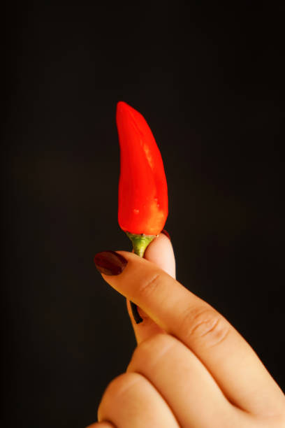 A cute brown-eyed blonde woman bites nervously into a scarlet chili pepper, worried about the burning heat. 