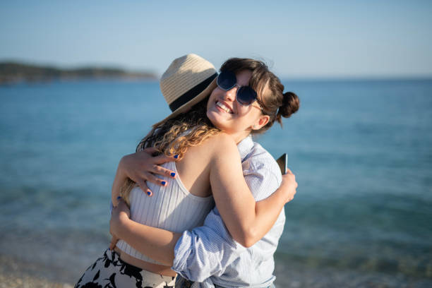 Happy female friends embracing on the beach at sunset on their summer vacation.
