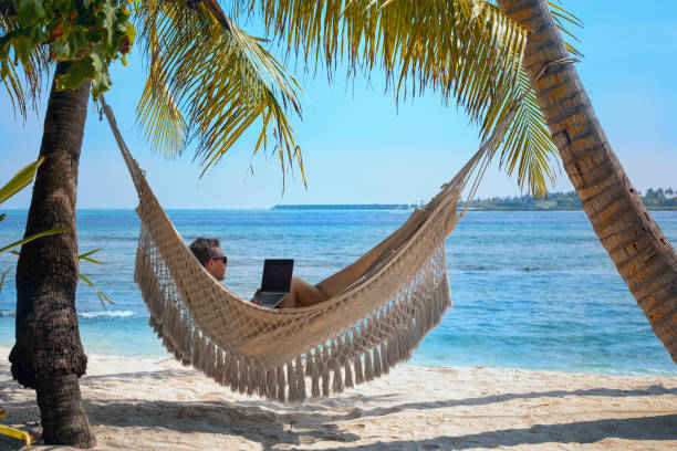 istock man working on laptop computer while relaxing in beach hammock, freelance worker, remote job 2153124723