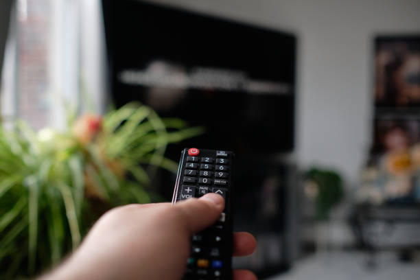 istock man is holding a TV remote while selecting a program on the flat screen TV in the livingroom 2153134181