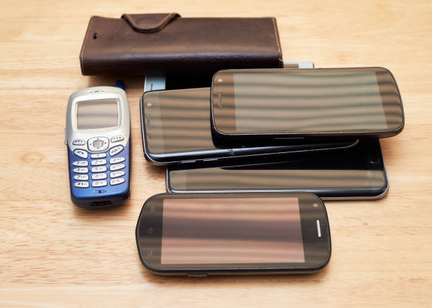 a bunch of old used up cell phones from different decades piled up on the table