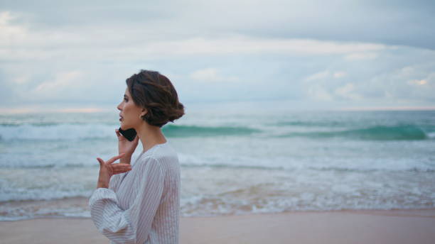 istock Woman enjoying cellphone conversation at ocean waves. Calm model stepping beach 2153136096