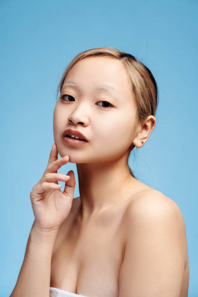 istock Calm Asian girl with bare shoulders looking at camera, holding hand on cheek, vertical 2153143644