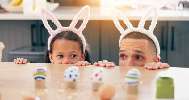 istock Child, father and easter with eggs, happy or thinking at table for game, festive holiday or celebration. Dad, kid and bunny ears for rabbit costume, ideas or playful for love, bonding and family home 2153148358