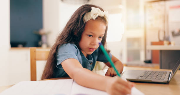 istock Girl, learning and writing with pencil, homework and book for development, knowledge and thinking at desk. Child, student and notebook by laptop for education, problem solving or notes in family home 2153148367