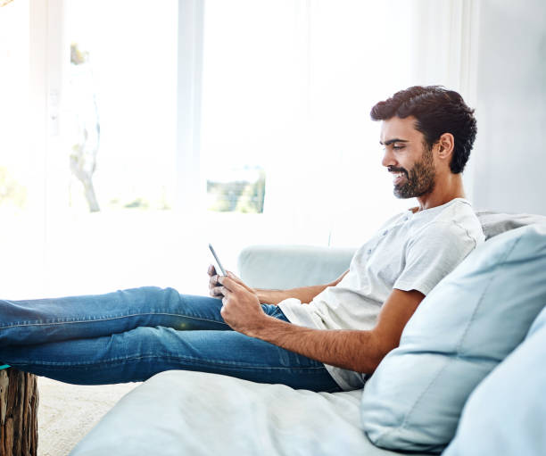 istock Home, man and tablet on sofa for networking, chat and online conversation with contact. Living room, male chatter and mobile app for streaming movies, games and social media with technology to relax 2153154314