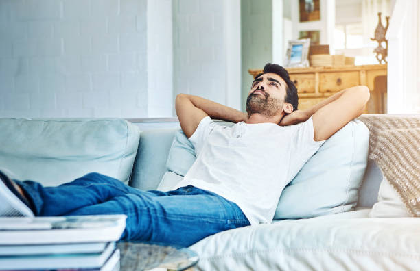 Feet up, wind down hombre, relájese y acuéstese en el sofá para la satisfacción, la tranquilidad y el descanso de fin de semana en la sala de estar. persona perezosa, tranquila y masculina con los brazos extendidos en el sofá para la felicidad, el descanso cómodo o el
