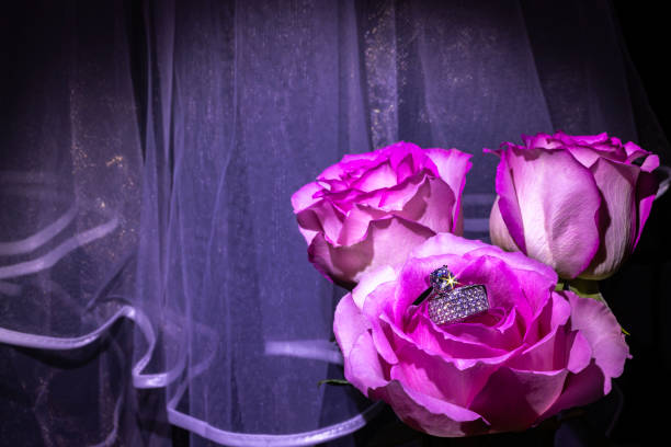 A pink heart-shaped gift box and a pair of wedding rings on a background of flowers. Wedding gift concept. Gift concept for Valentine's Day.