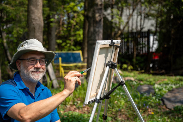 Mature man painting on canvas while in backyard during springtime day