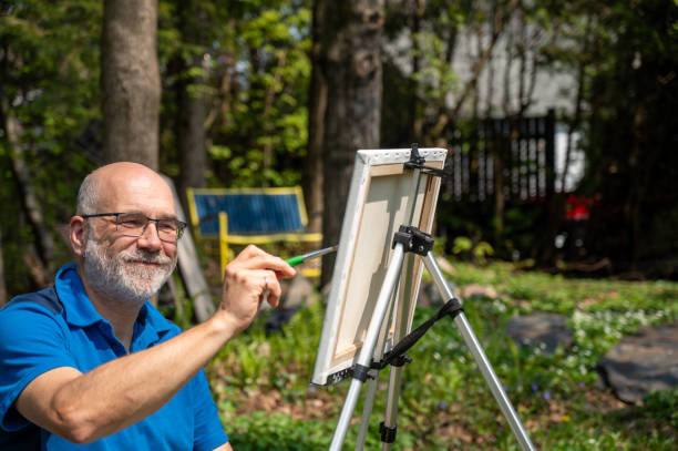Mature man painting on canvas while in backyard during springtime day