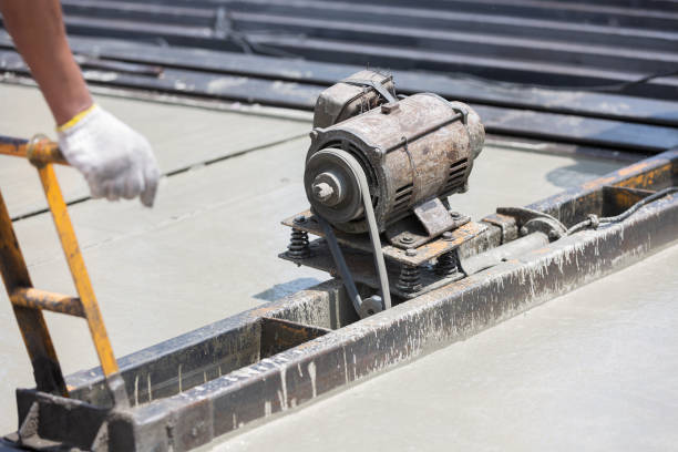 Construction worker operating machine spreading wet concrete pouring at precast concrete wall construction site. Worker or mason working or making smooth surface of concrete with machine at site work