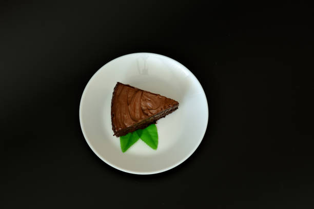 istock A piece of biscuit layer cake with chocolate and mint leaves on a white ceramic plate on a black background. 2153166491