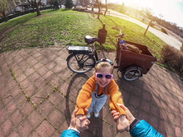 A man is helping a child ride a bike. The child is wearing a helmet. The bike is parked in a grassy area