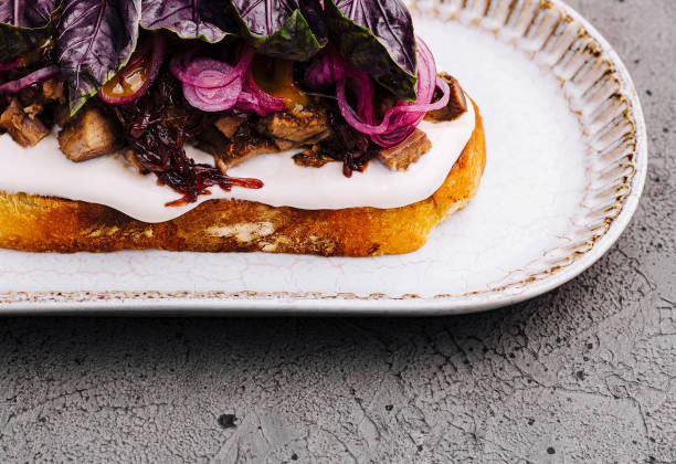 Artisanal toast topped with cream cheese, caramelized onions, and fresh purple basil on ceramic plate