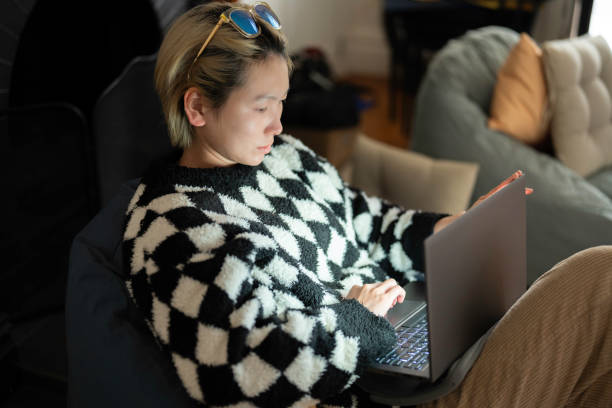istock Asian woman using laptop while sitting on bean bag at home 2153188565