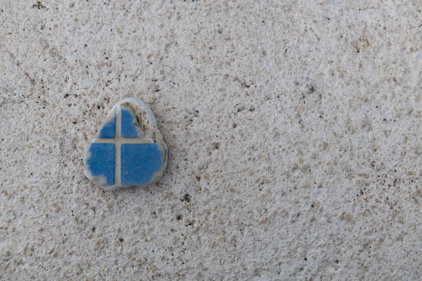 Small cross etched in afragment of broken blue tile on a white textured background.