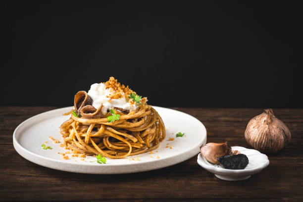 Black fermented garlic linguine pasta with  fermented garlic sauce and dry grated bread. A simple recipe in 10 minutes. Modern recipes for Italian pasta, gourmet soft taste. Rustic style, magic light, front view