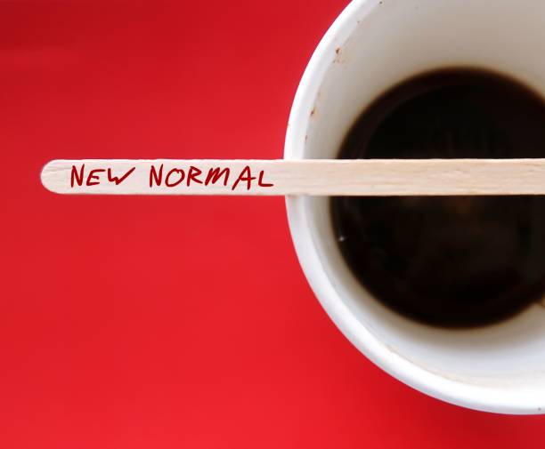 Coffee disposable stirrer on paper cup with text written NEW NORMAL,  state to which economy or society settles following crisis which differs from prior situation, especially post pandemic