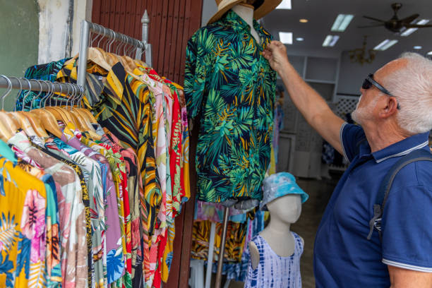 Man Examining Tropical Shirts at Market Stall A man in sunglasses examines a tropical shirt on a mannequin at an outdoor market stall. He looks through the vibrant shirts, enjoying a casual and detailed shopping experience. colorful check shirts on sale at a clothing store stock pictures, royalty-free photos & images