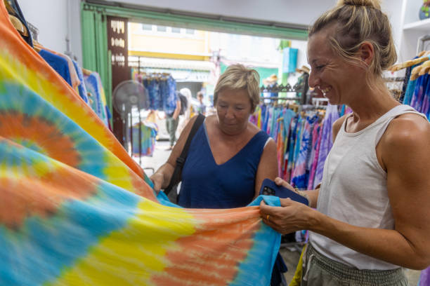 Women Admiring Colorful Tie-Dye Fabric in Boutique Two women in a boutique shop, smiling and examining a bright tie-dye fabric, enjoying their shopping experience. colorful check shirts on sale at a clothing store stock pictures, royalty-free photos & images