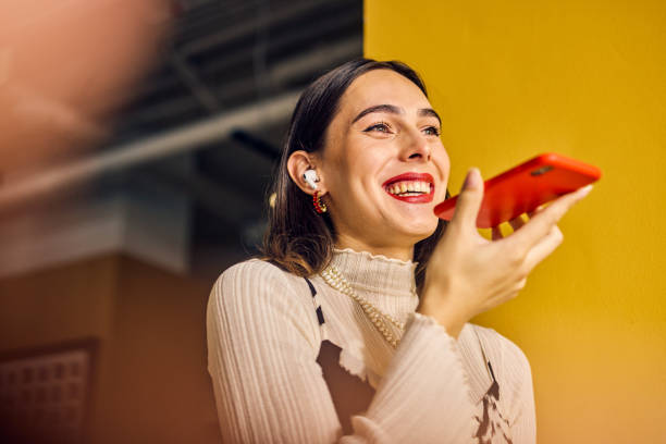 istock Smiling Transgender woman using voice assistant on smartphone in a colorful office. Technology and communication in business concept 2153221859