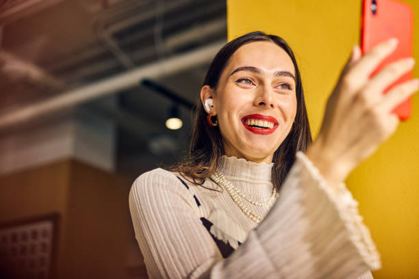 istock Smiling Transgender woman using voice assistant on smartphone in a colorful office. Technology and communication in business concept 2153221863