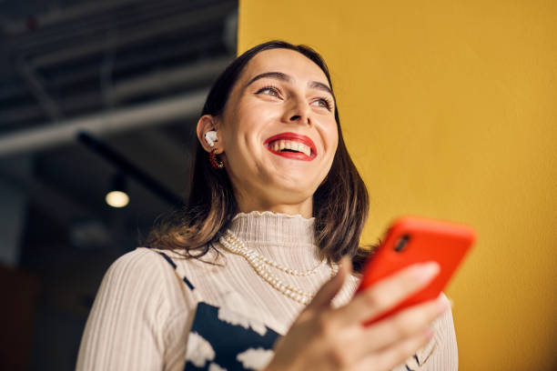 Smiling Transgender woman using voice assistant on smartphone in a colorful office. Technology and communication in business concept