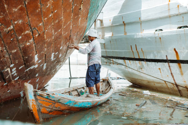 A worker in a body protective suit paints the hull of a sailing yacht with spray.