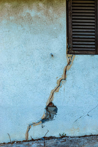 A close-up of a white concrete wall featuring a prominent vertical crack and a rough textured surface. The minimal design conveys a sense of aging and imperfection, making it suitable for use in architectural, industrial, or abstract compositions.