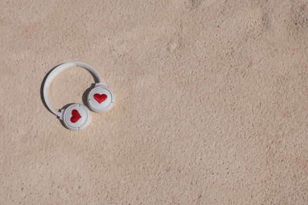 White headphones with hearts on the sand. Top view, copy space