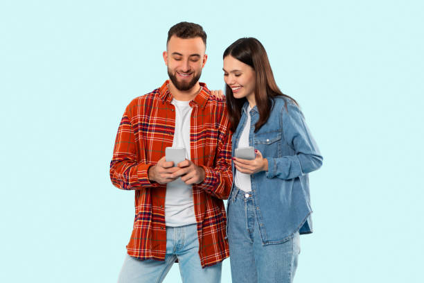 istock Couple smiling while holding smartphones on blue background 2153233165