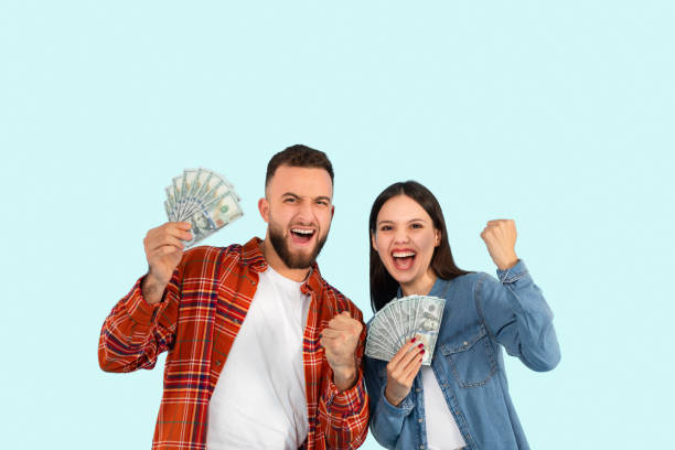 istock Excited couple holding cash with joy on blue background 2153233204