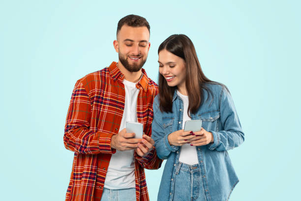 istock Cheerful young couple posing with smartphones on blue studio backdrop 2153233207
