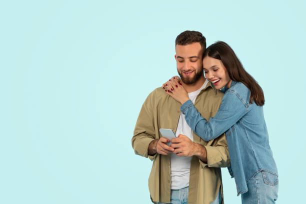 istock casual couple chatting on smartphone embracing against blue studio backdrop 2153233302