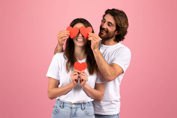 istock Joyful couple playfully covers their eyes with red paper hearts, sharing a light-hearted moment together 2153233393