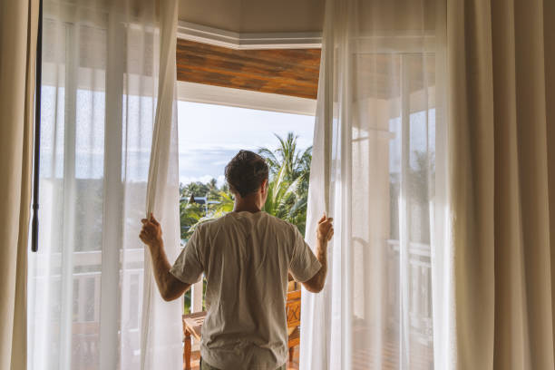 Man Opening Curtains to Tropical Balcony View