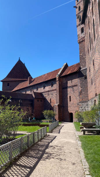 istock Charming old brick building with a tower and garden on a sunny day. Historic architecture with lush greenery and blue sky 2153237404