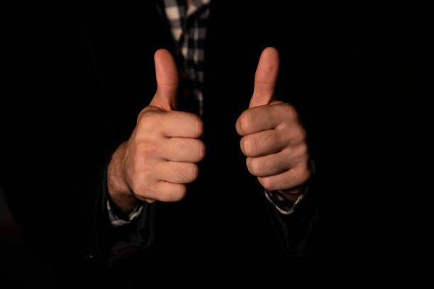 a man with both hand thumbs up pose in a black background with an executive look